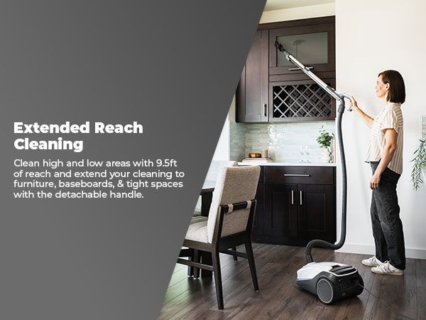 Person using a vacuum with an extended reach in a kitchen setting.