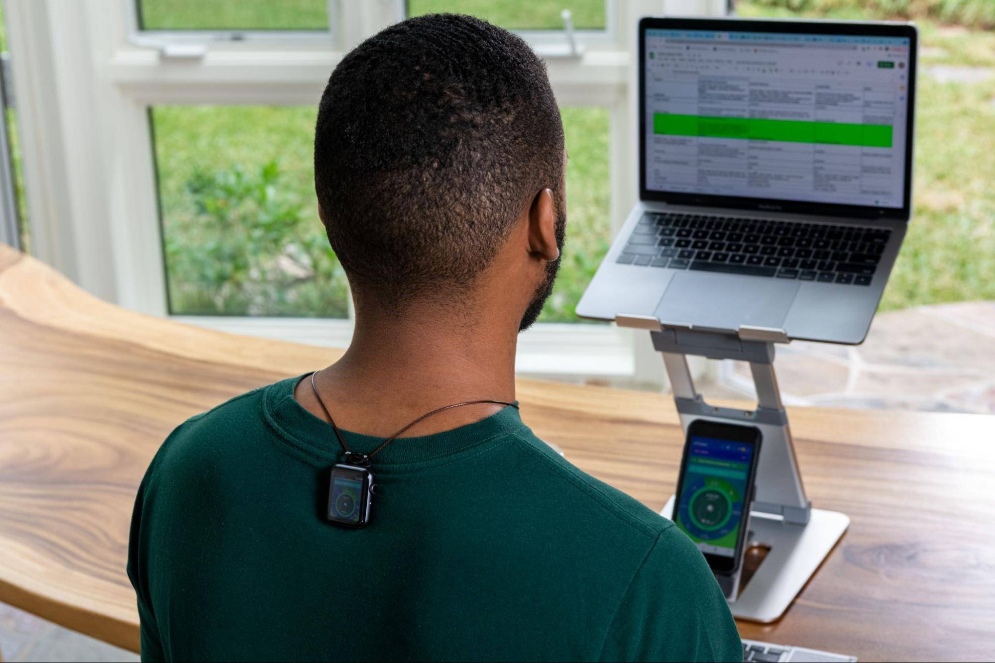 Man working on laptop with phone tracking posture from Apple Watch place on upper back