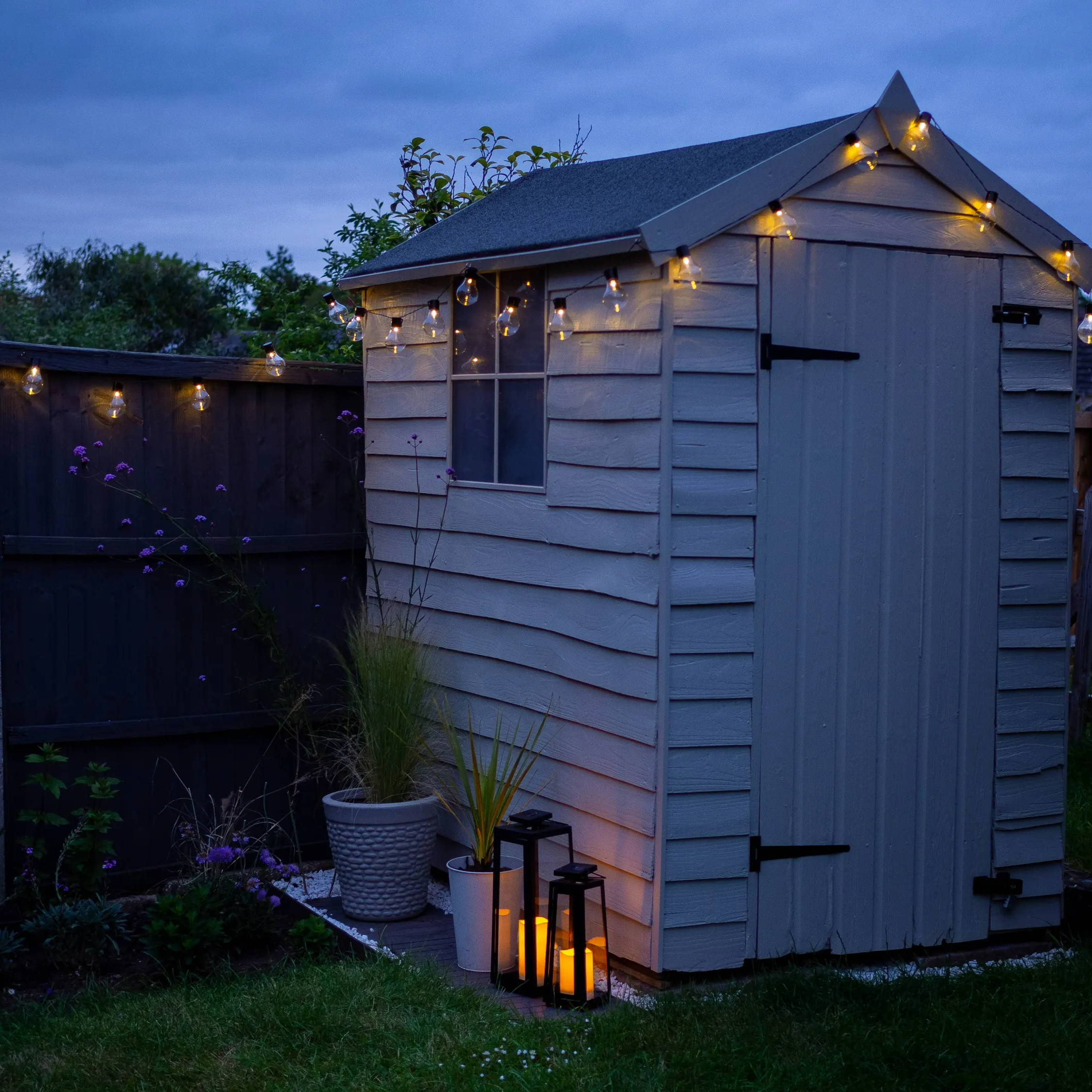 Photo of garden at night with lit up solar lanterns and solar festoon lights.