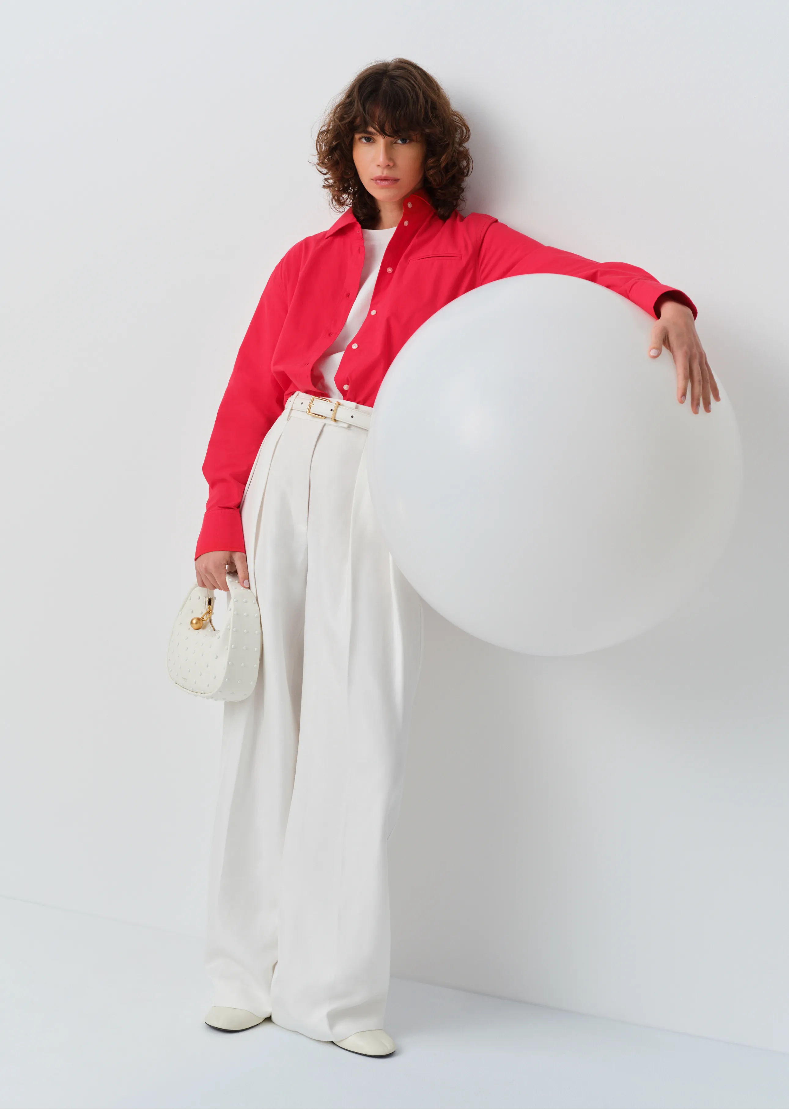 Person in a red shirt and white pants holding a large white balloon.