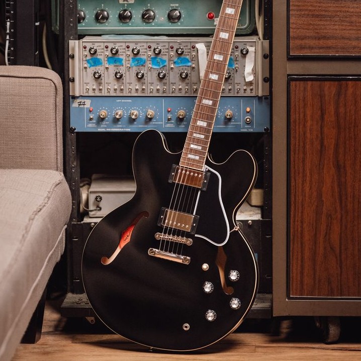 Black electric guitar leaning against audio equipment in a studio setting.