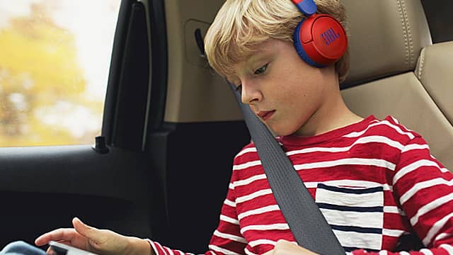 A boy wearing headphones, seated in a car, focused on a device.