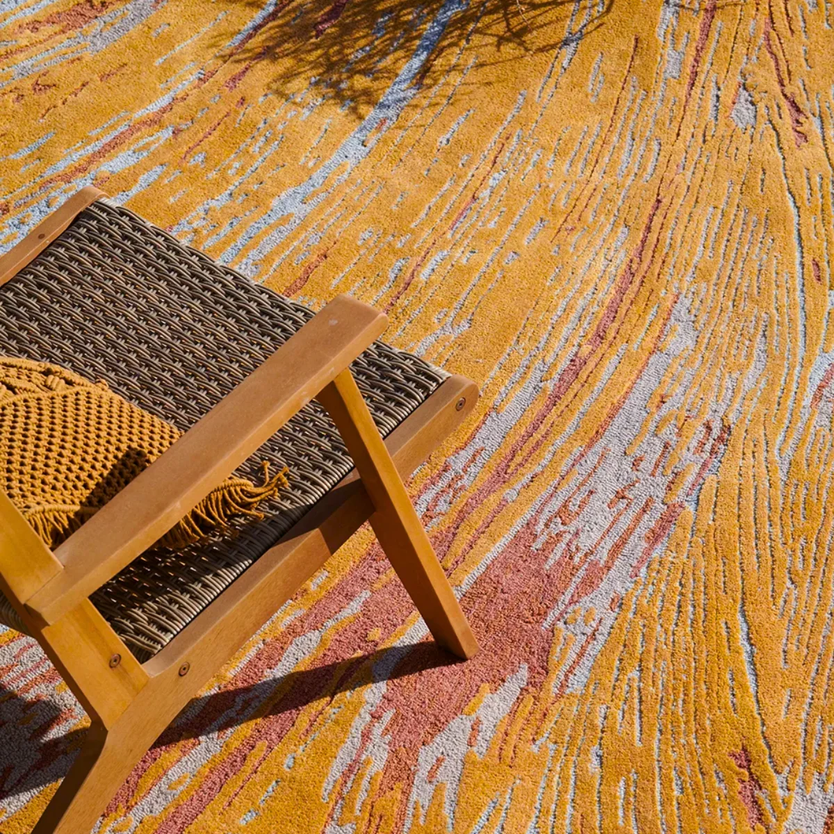  Close-up of a colorful textured outdoor rug with abstract pattern beneath a lounge chair, showcasing fade-resistant performance fibers for sunny patios.