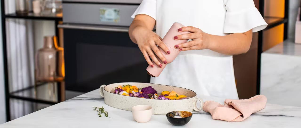 woman using grinder on root vegetables to be roasted