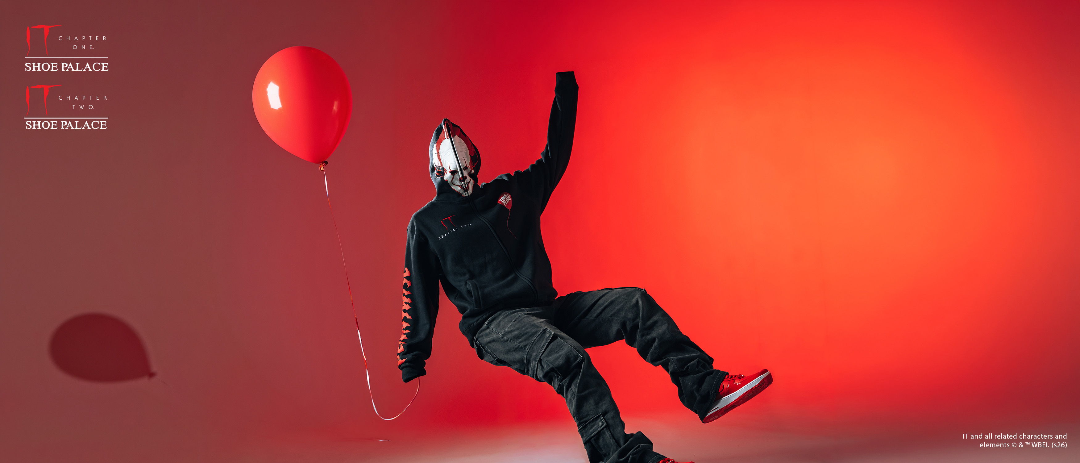 Person in a black outfit holding a red balloon against a red background.