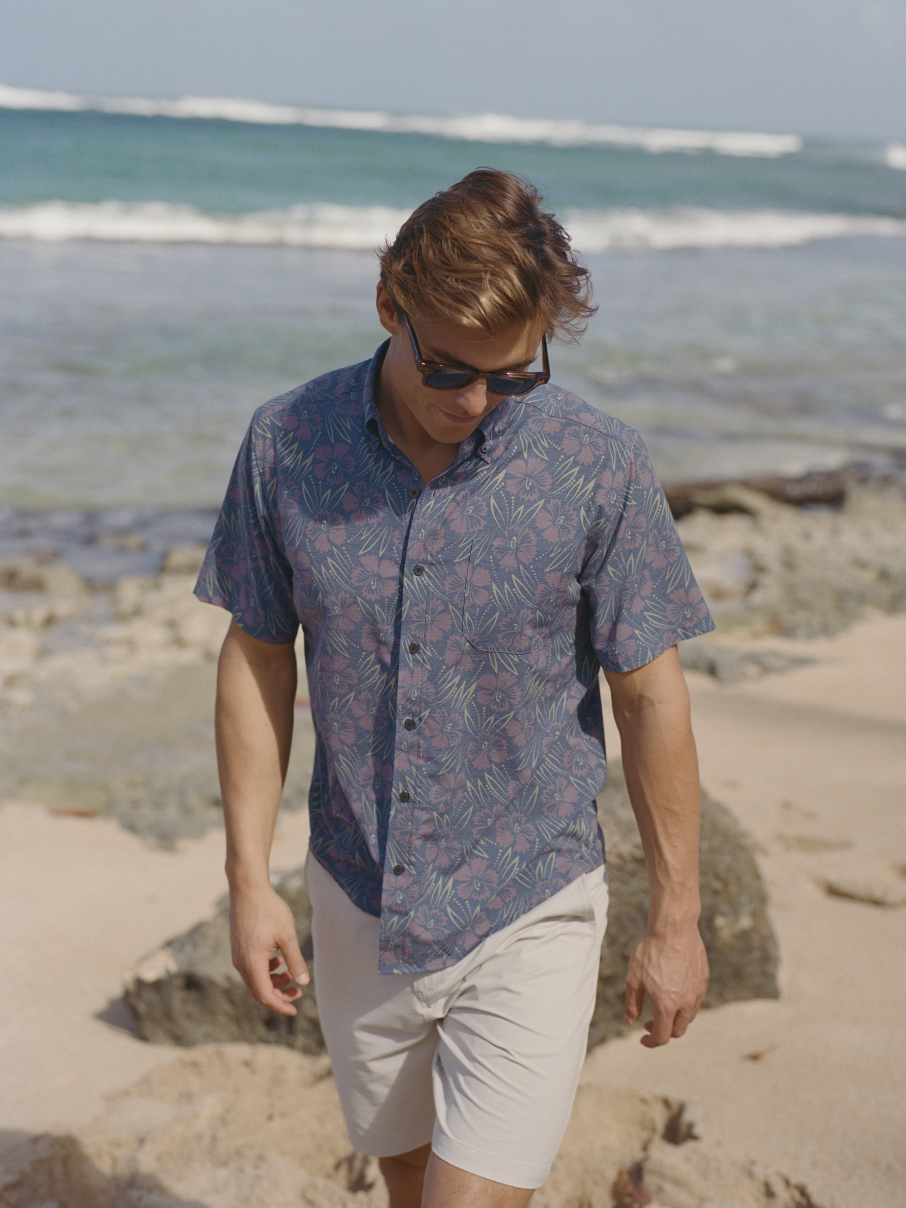 A man in sunglasses walking on the beach near the water.
