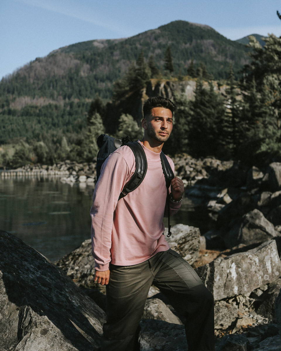 A man hiking in the wilderness with a salmon color long sleeve t-shirt and a backpack.