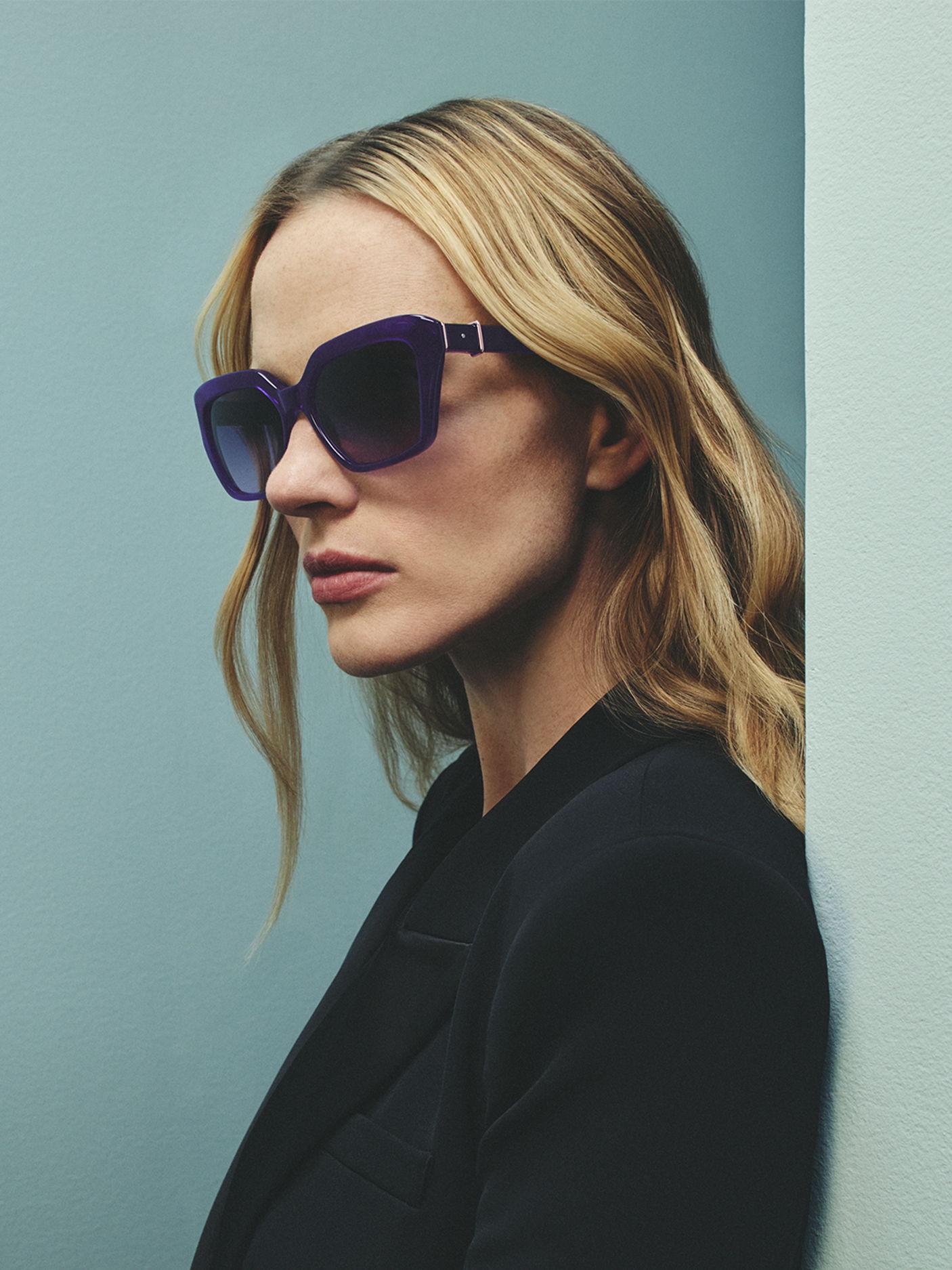 A woman with long hair wearing Robert Marc sunglasses against a blue background.
