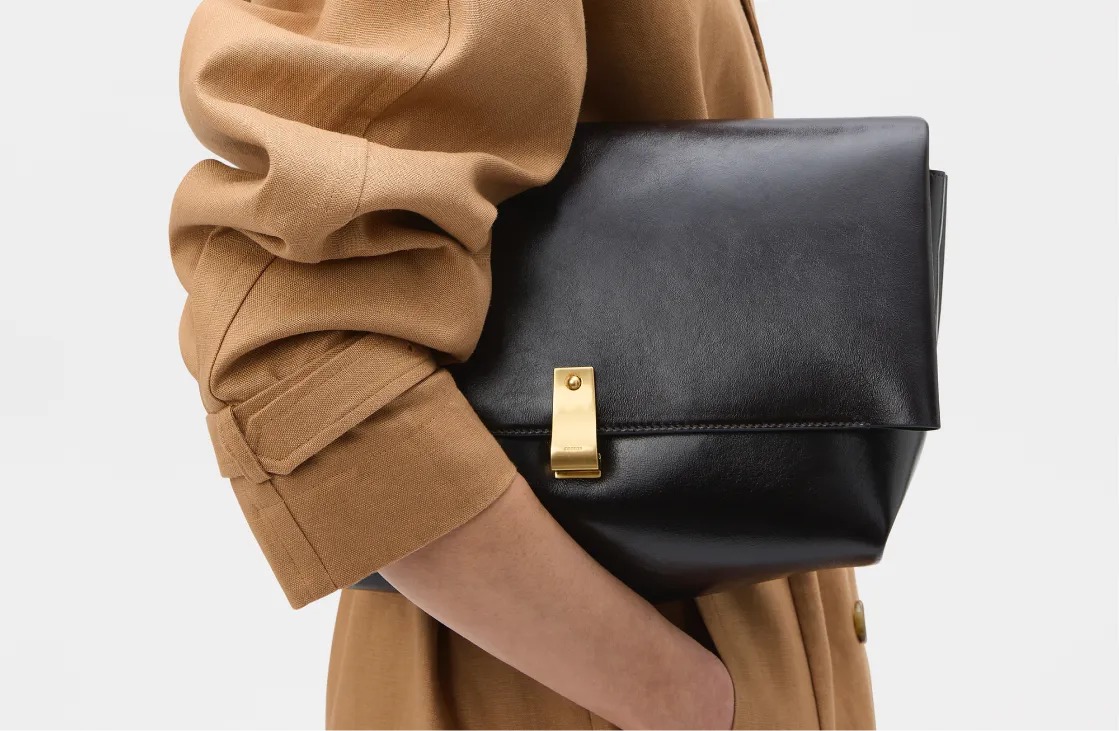 A person holding a black leather clutch bag.