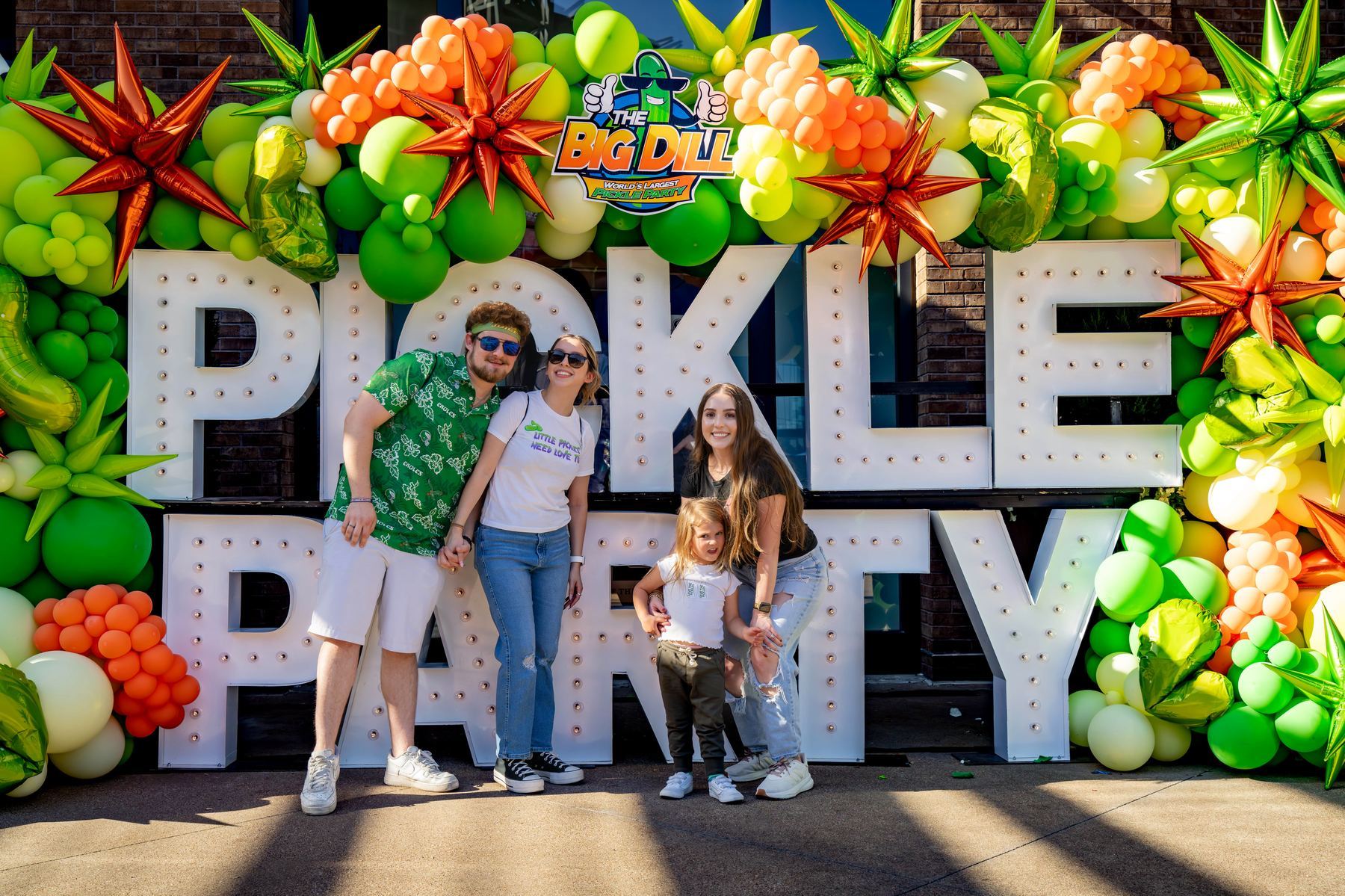 Family group posing at the PICKLE PARTY marquee letters with the official Big Dill logo and balloon installation at The Big Dill Arlington Texas 2025.