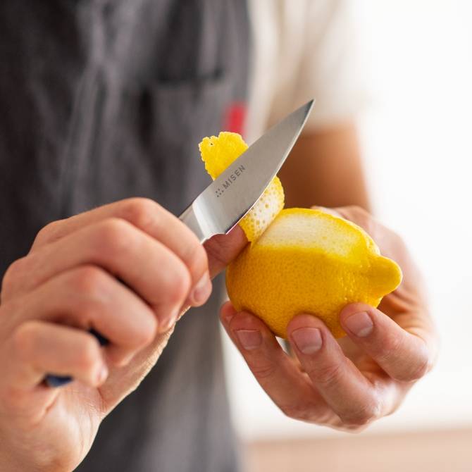 A chef uses a blue Misen Paring Knife to easily peel a lemon.
