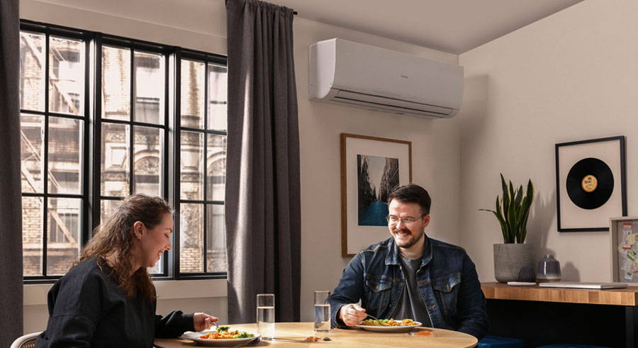 a couple eating at their kitchen table with a Haier ductless air conditioner on the wall behind them.