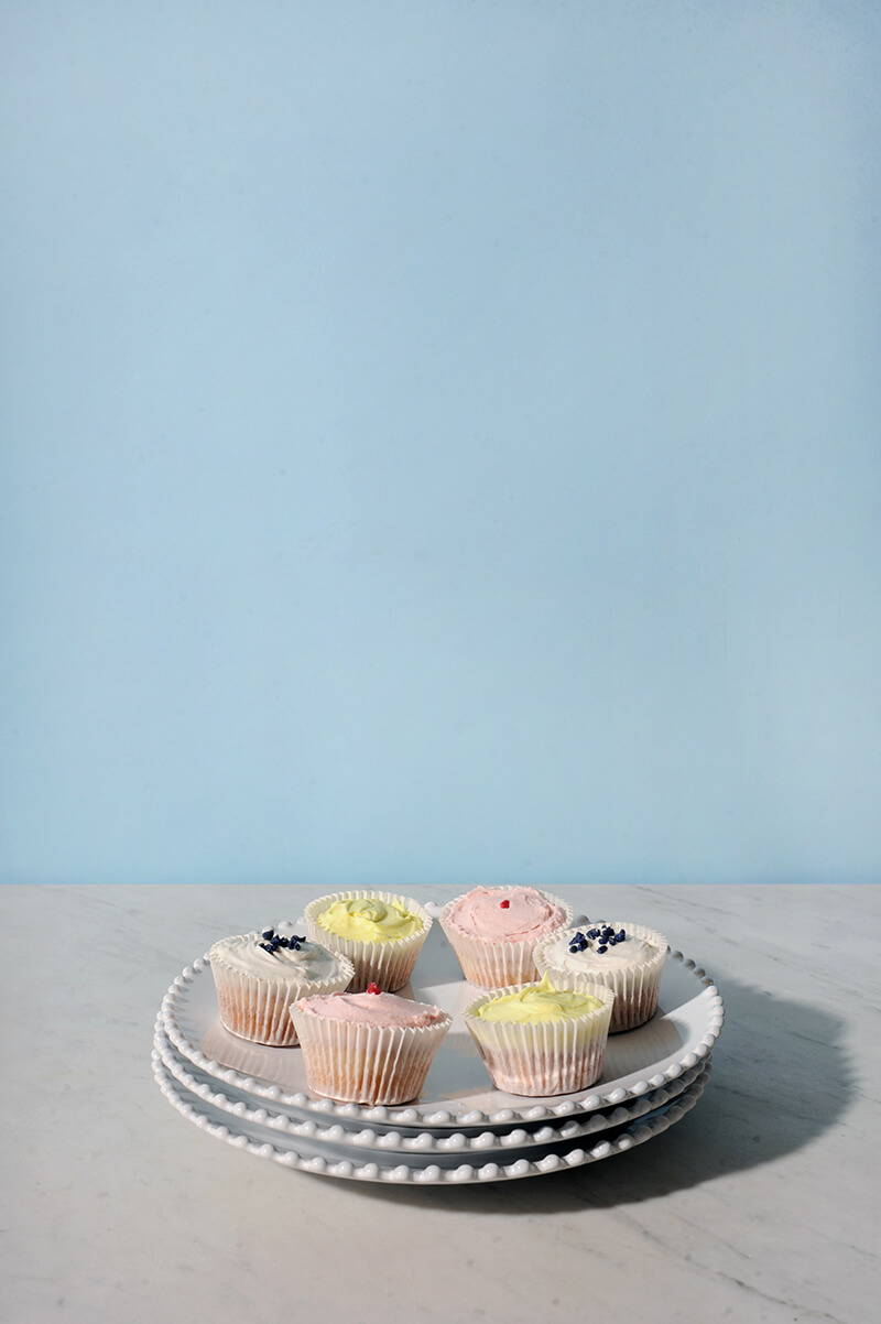 A stack of three pearl white dinner plates topped with assorted colourful cupcakes.