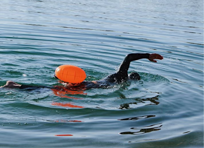 Ein Triathlet im Wasser mit einer orangenen Schwimmboje.