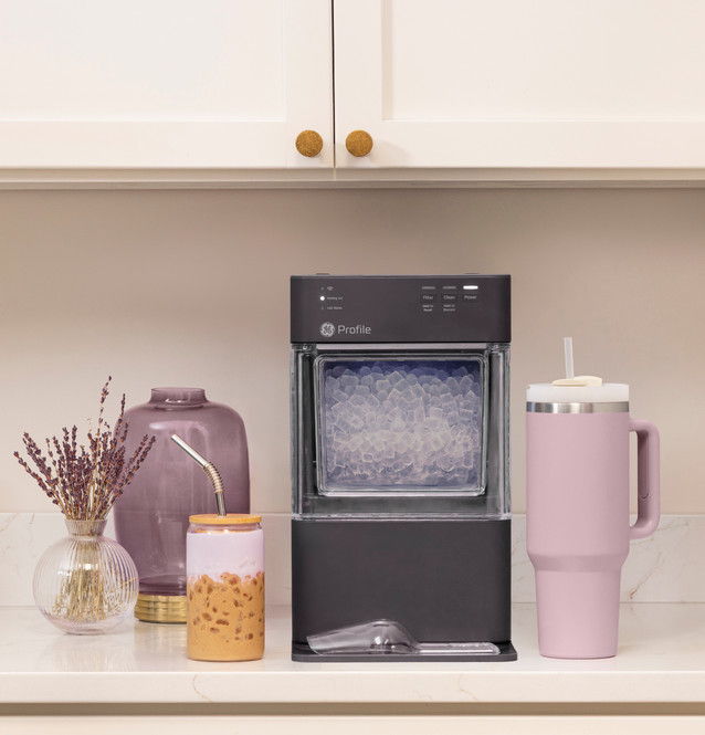 Ice maker on countertop with pink drinkware and decorative vase.