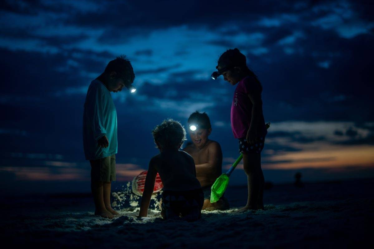 A group of young kids with headlamps playing on the beach