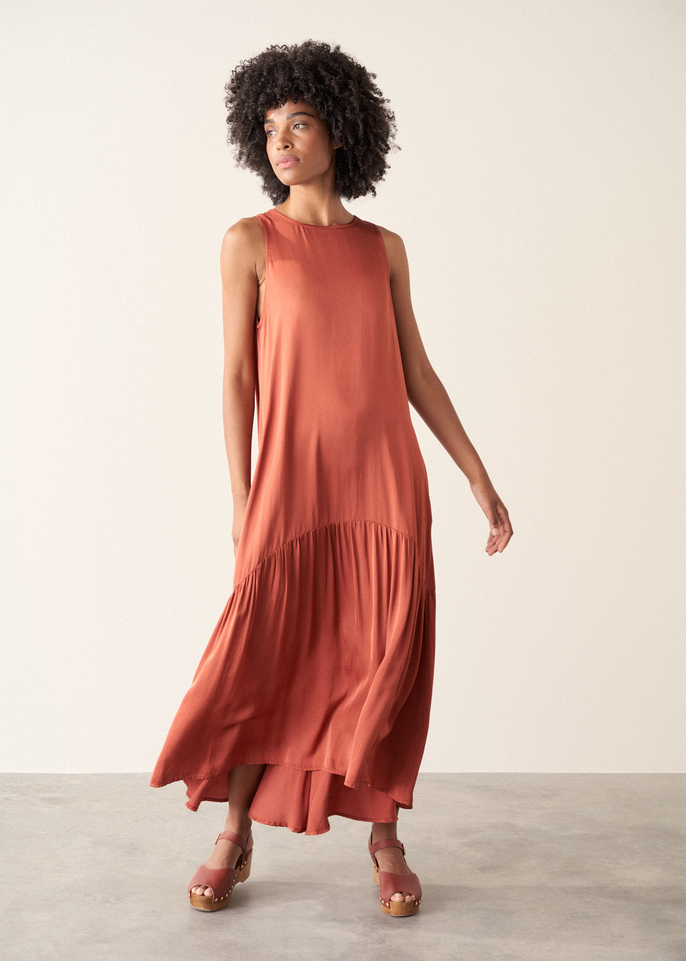 Woman wearing dark orange satin tiered floaty summer dress against a plain background