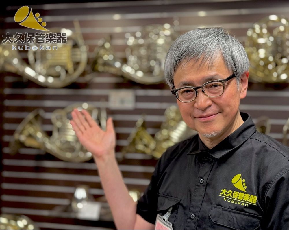 Person gesturing in front of musical instruments displayed on a wall.