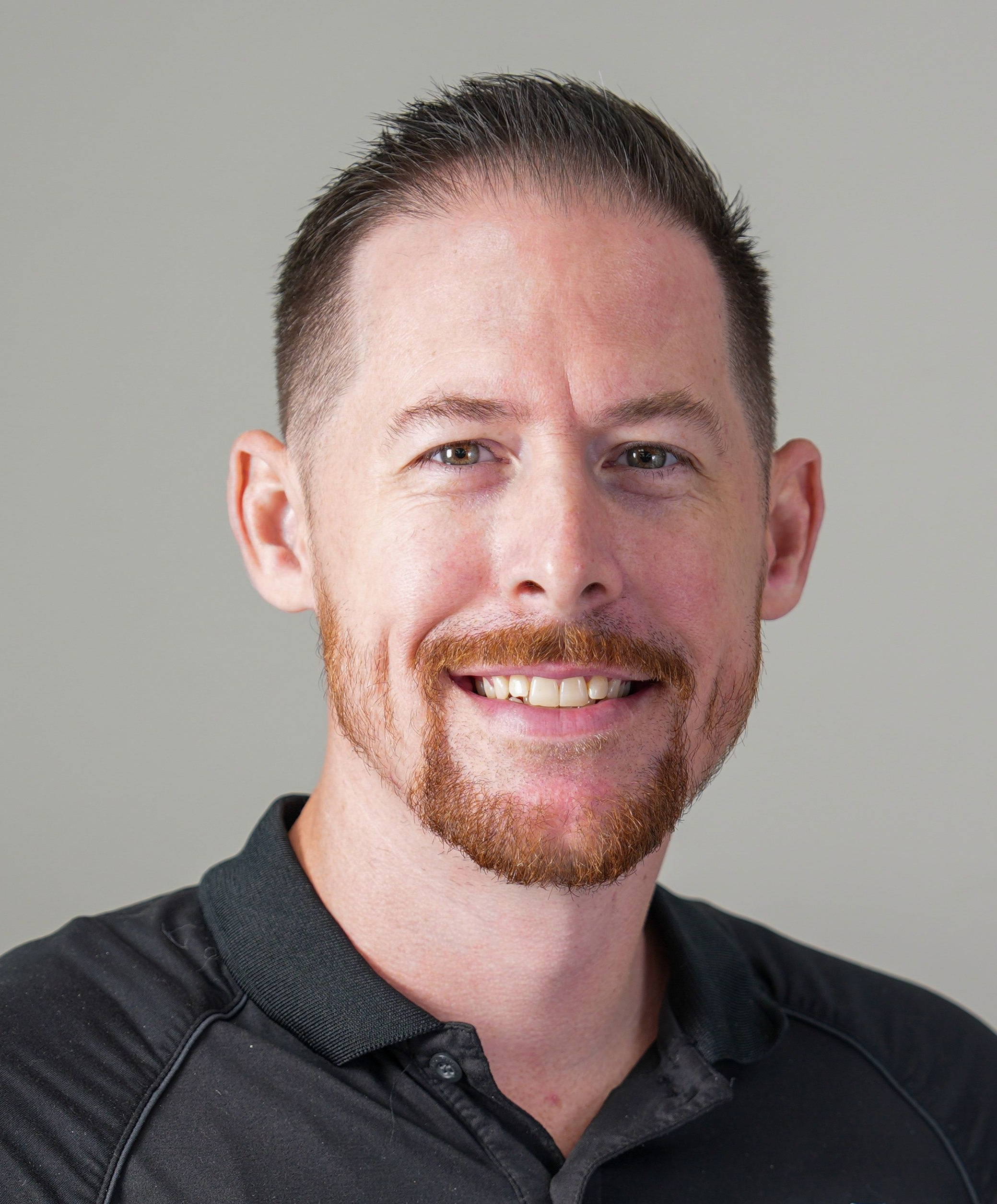 Smiling man in a black polo shirt against a gray background.