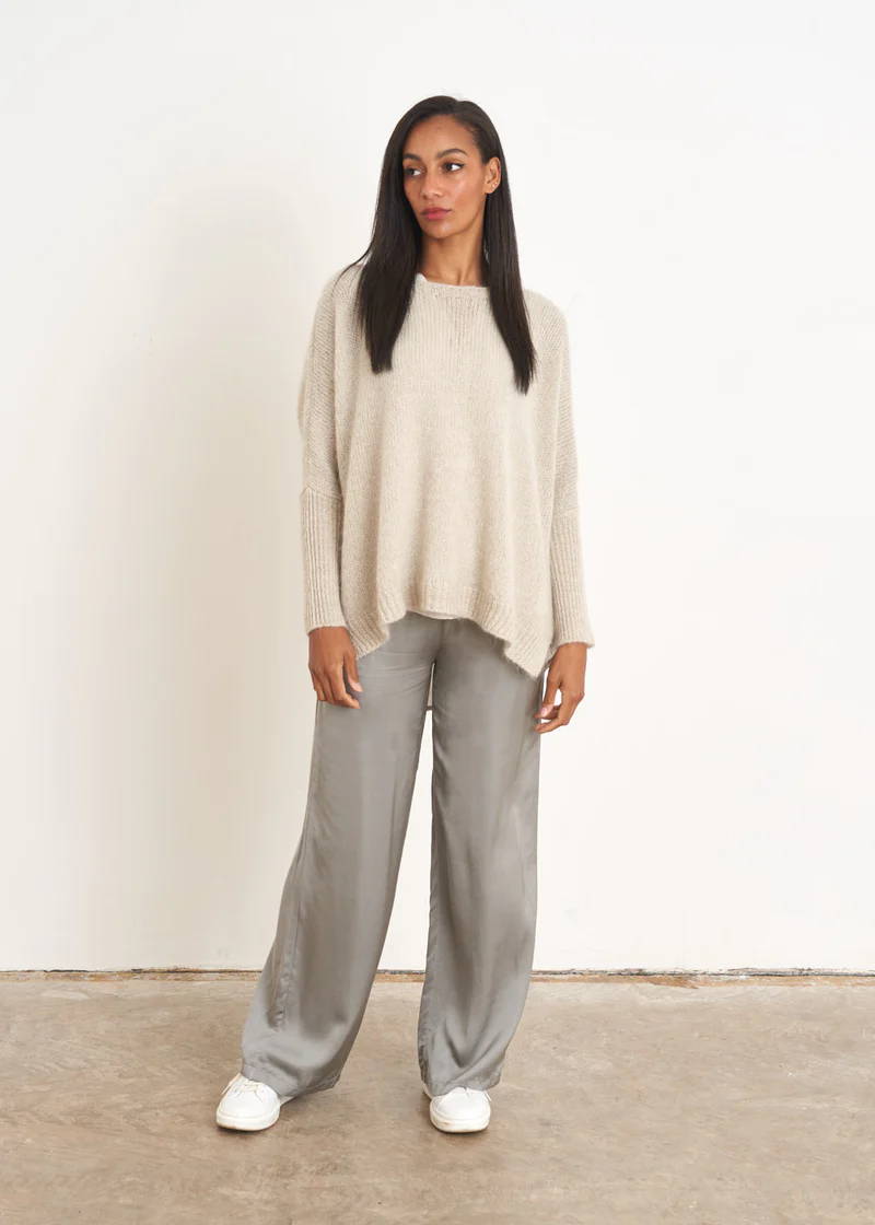 A model wearing a pair of sage green satin trousers with an off white slouchy knitted jumpers and white trainers