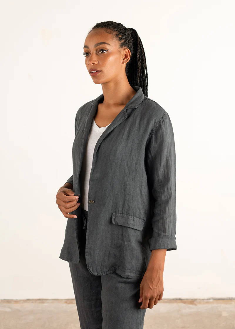 A model wearing a dark grey linen jacket over a white top and matching trousers