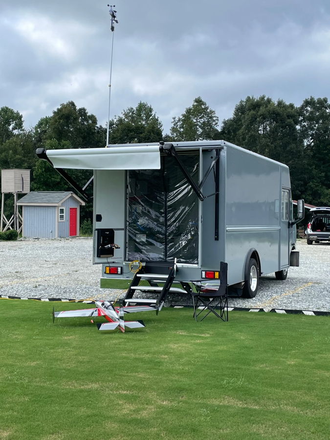 Grey step van with rear awning at RC airfield with red white and black RC plane on grass photo 4