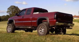 Red lifted GMC Sierra pickup side view in grass
