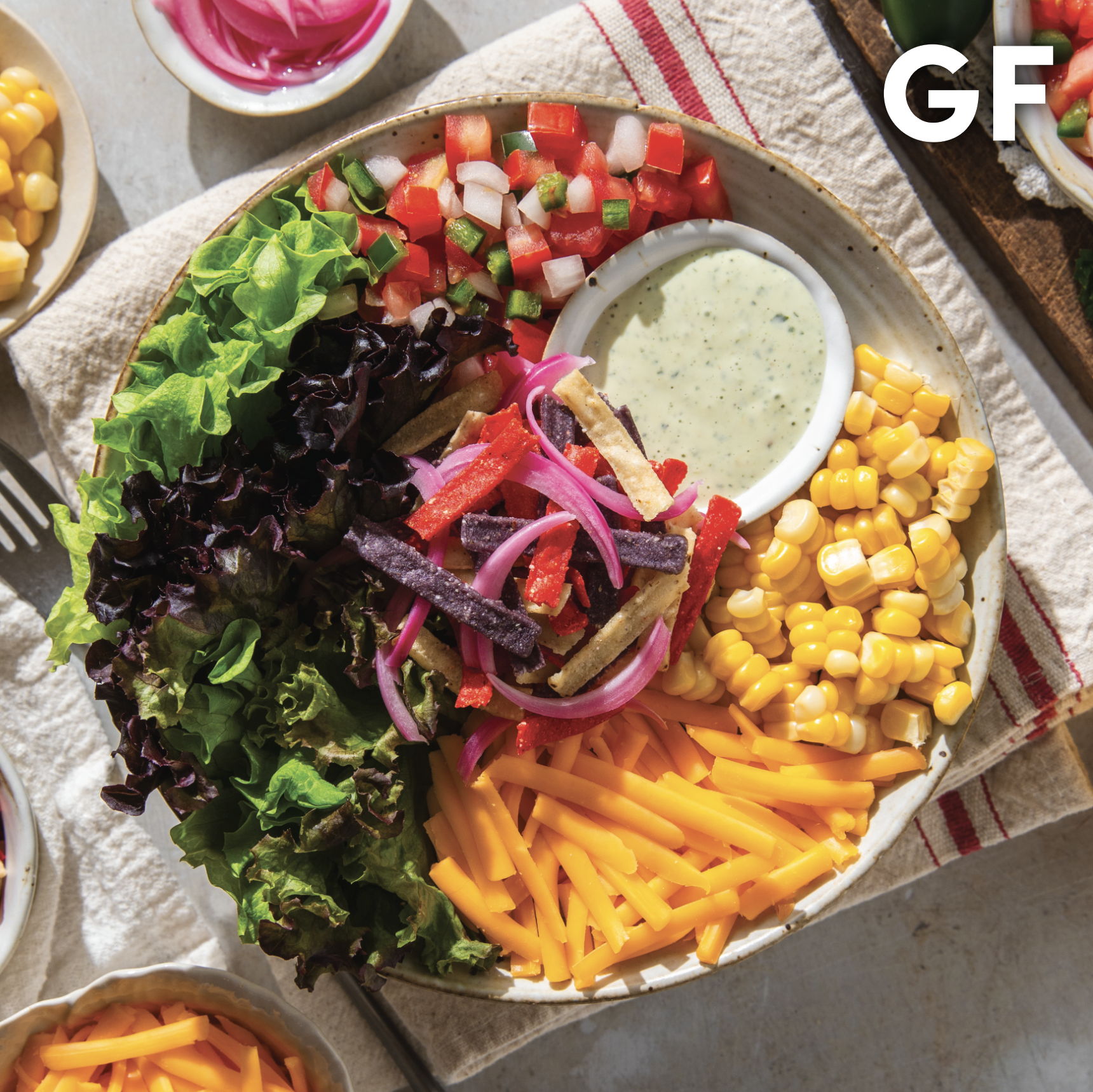 Colorful salad bowl with greens, corn, cheese, and dressing on a plate.