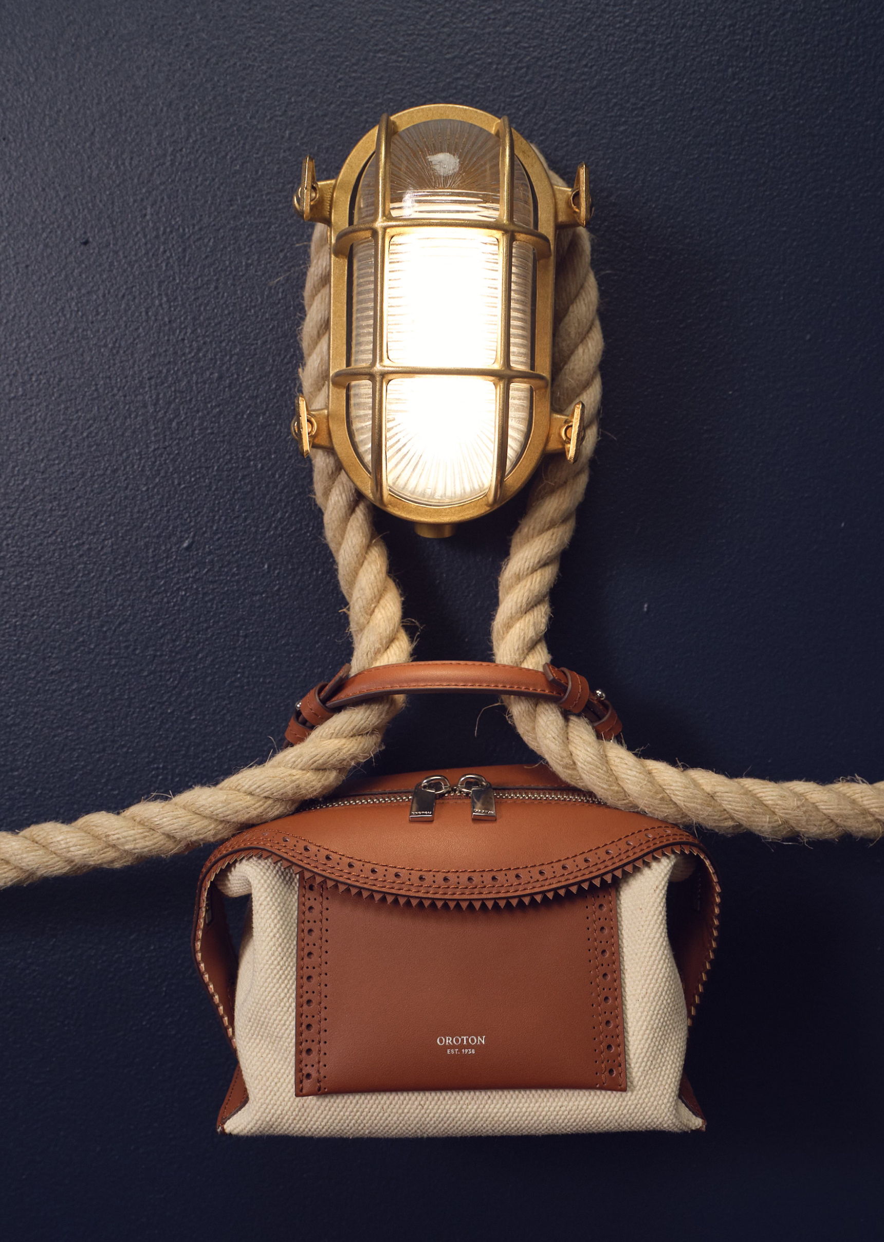A light fixture above a brown and white handbag tied with rope.