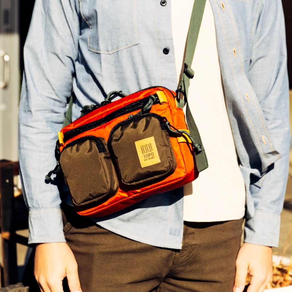 A person wearing a blue shirt with an orange messenger bag.