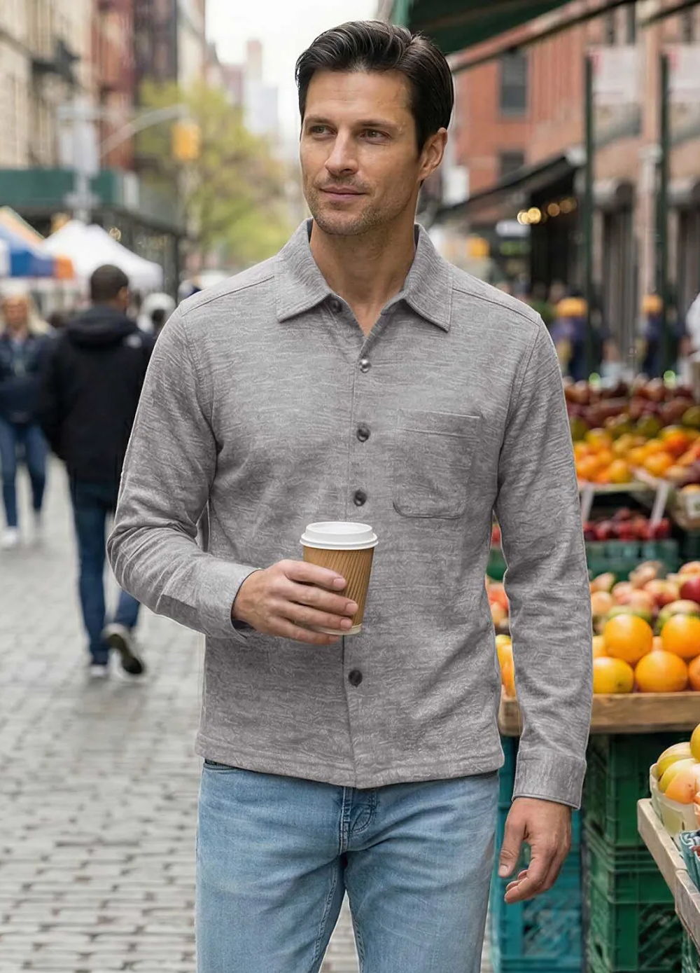 Man holding a coffee cup walking through a market with fruits.
