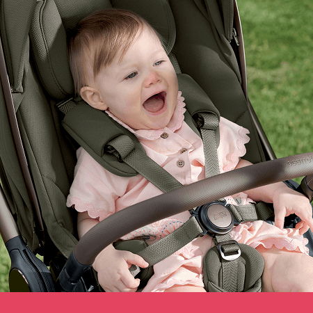 Baby in a stroller, smiling joyfully outdoors.