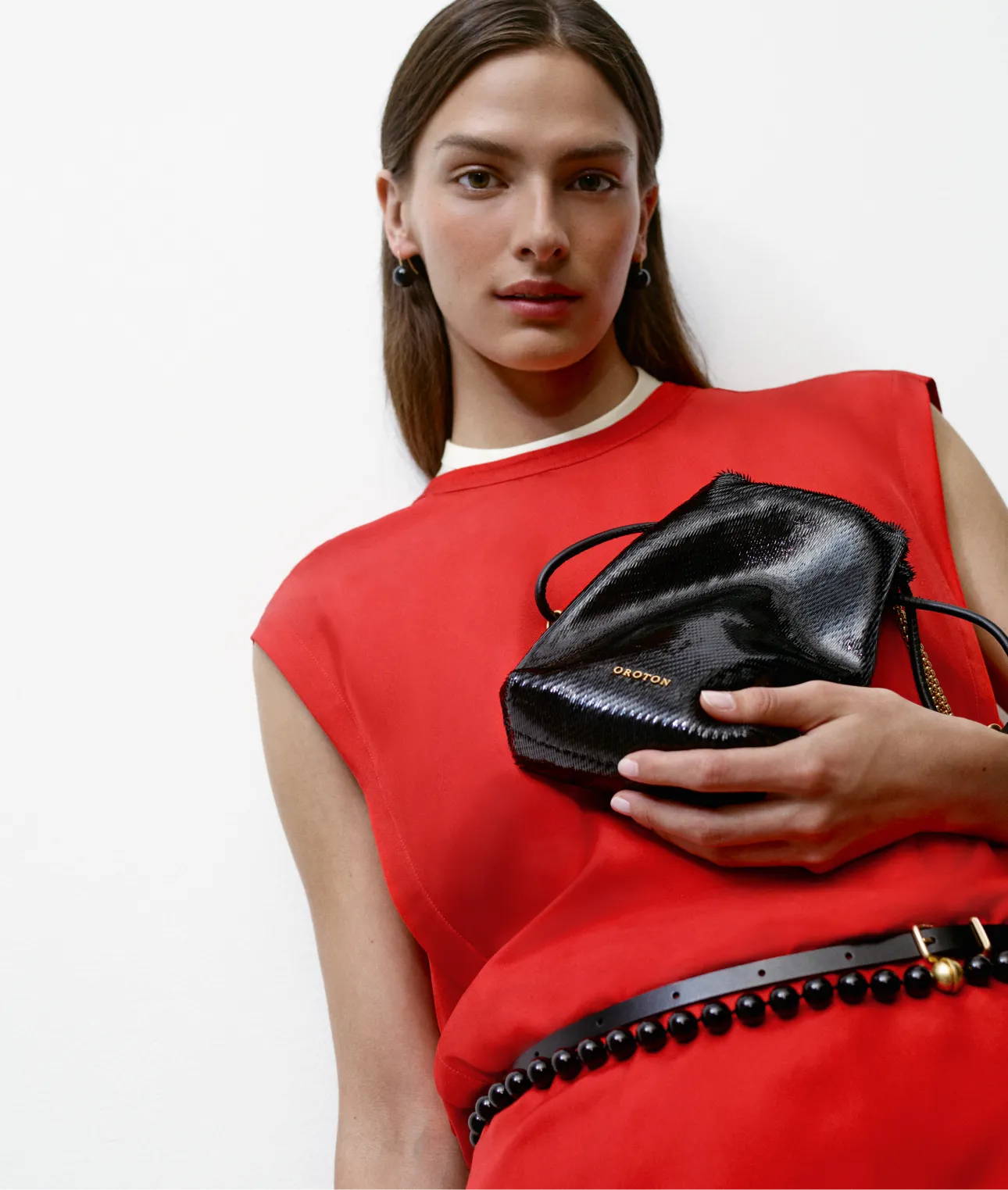 Model in a red outfit holding a black handbag against a white background.