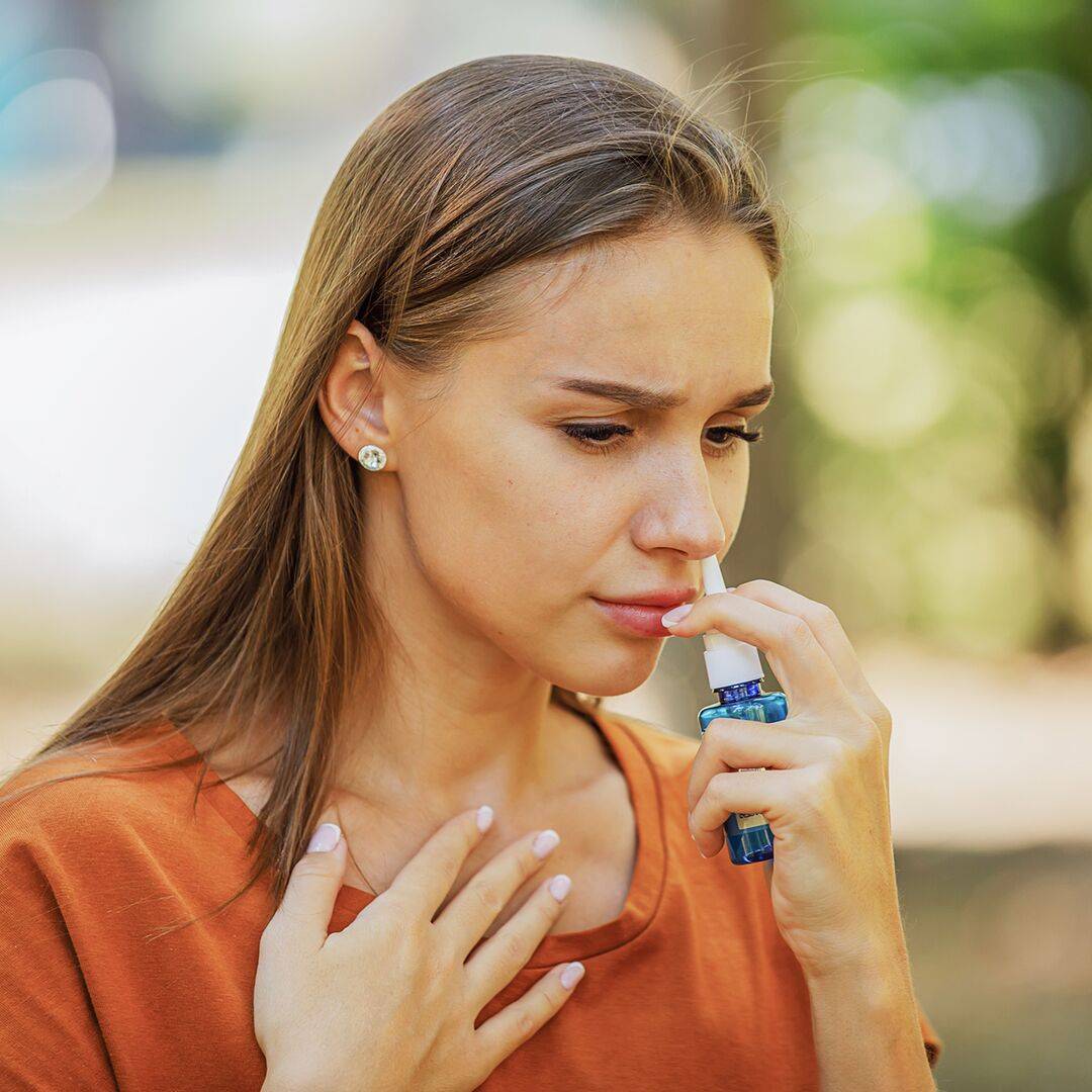 Mladá žena používající kortikosteroidní sprej během letního dne - to je častý krátkodobý způsob léčby alergické rýmy