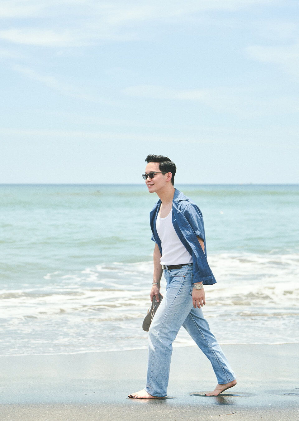 A person walking on the beach wearing casual attire and sunglasses.