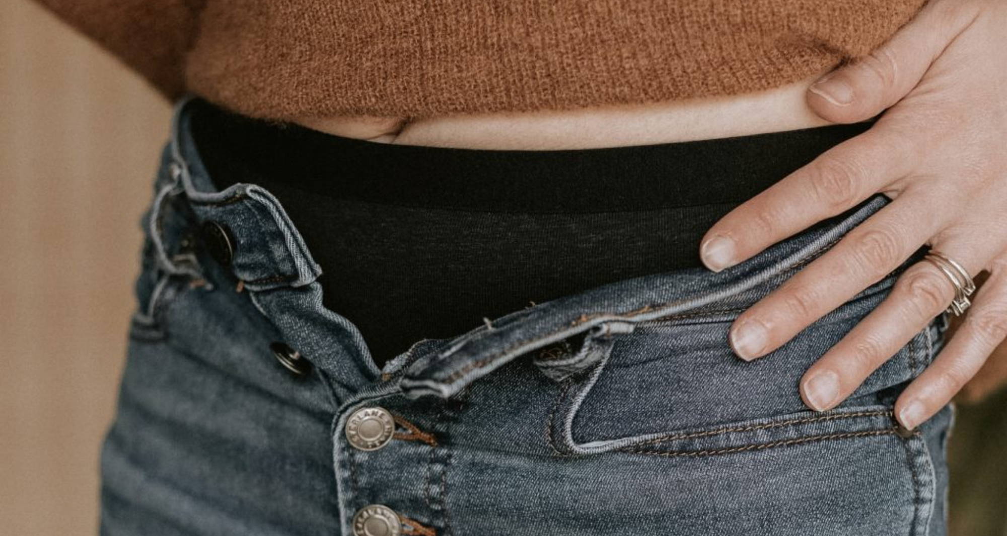 A woman with her left hand on her hip, and jeans buttons open showing her breathable underwear