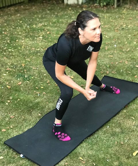 A woman in KYMIRA gear has a wide stance whilst lunging. 