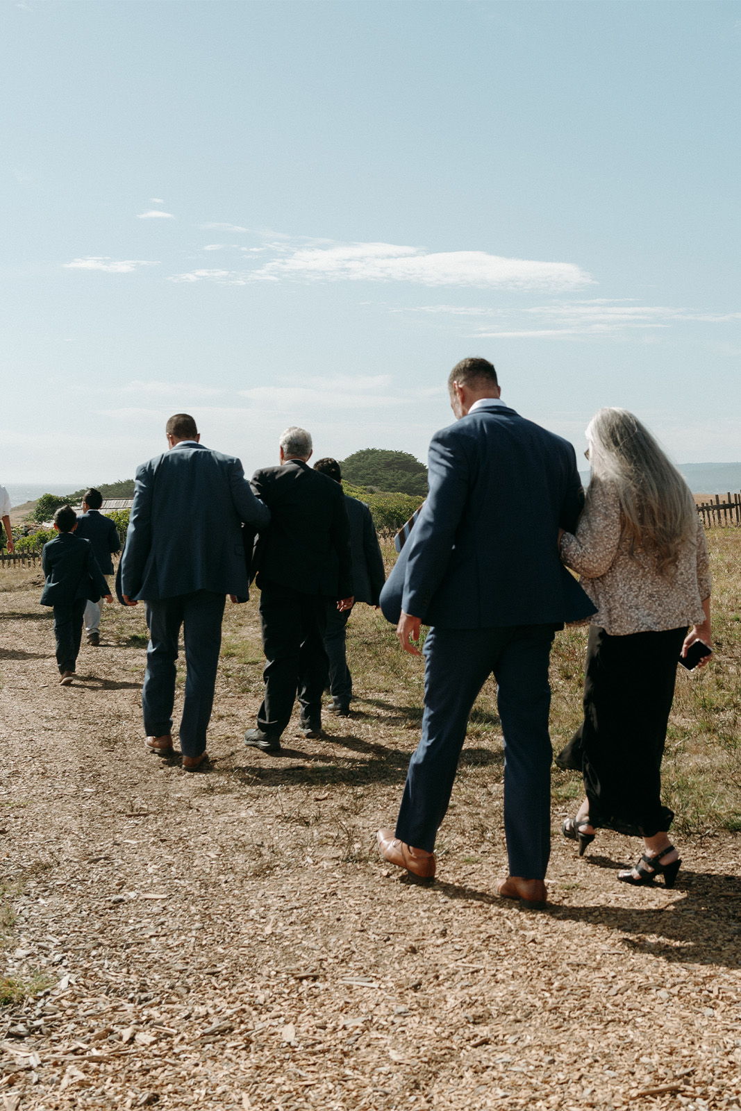 A group of people walking down a dirt path in formal attire.