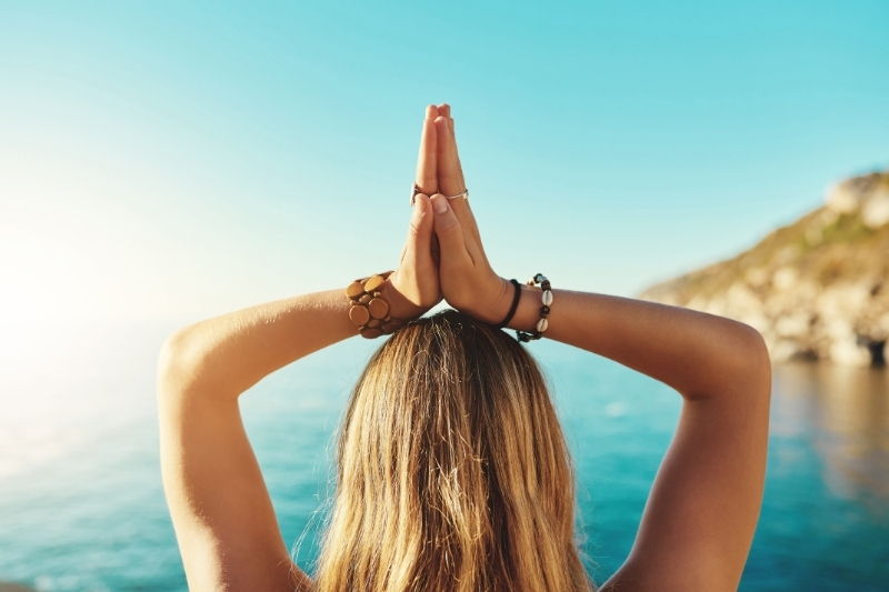Person with hands raised in prayer position by the water.