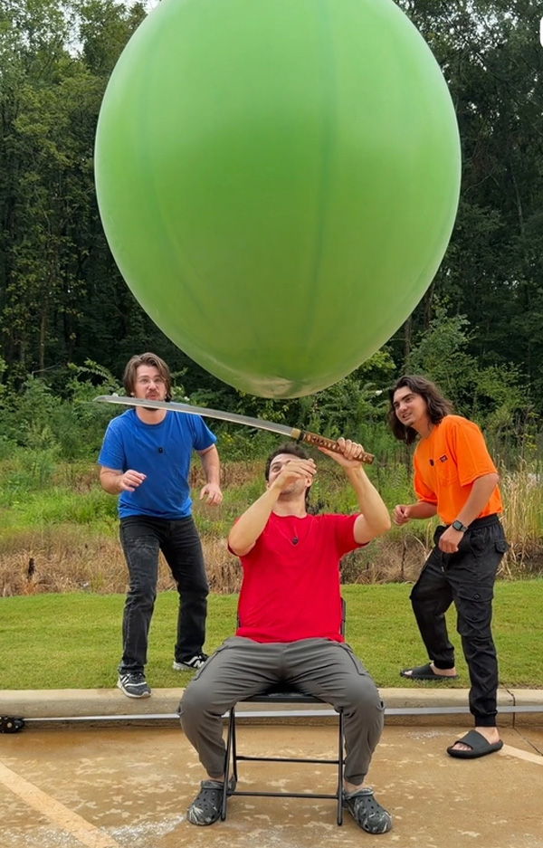 Three people play with a large green balloon outdoors.