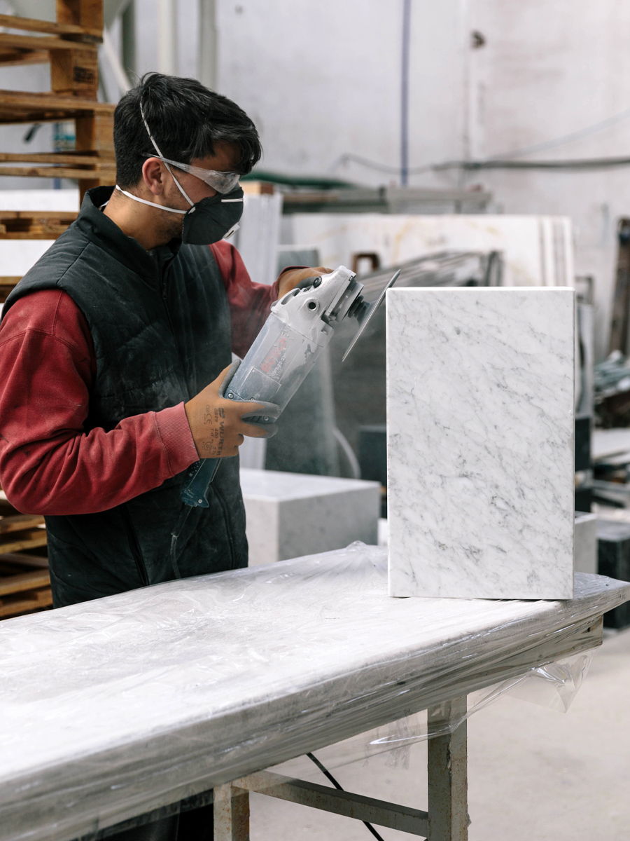 Worker shaping a block of plinth marble in a workshop.