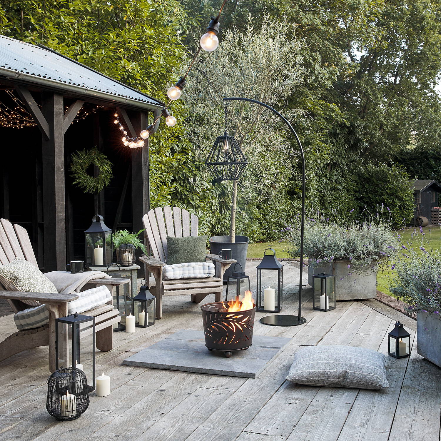 Outdoor firepit set up with garden furniture on decking, illuminated by festoon lights and more