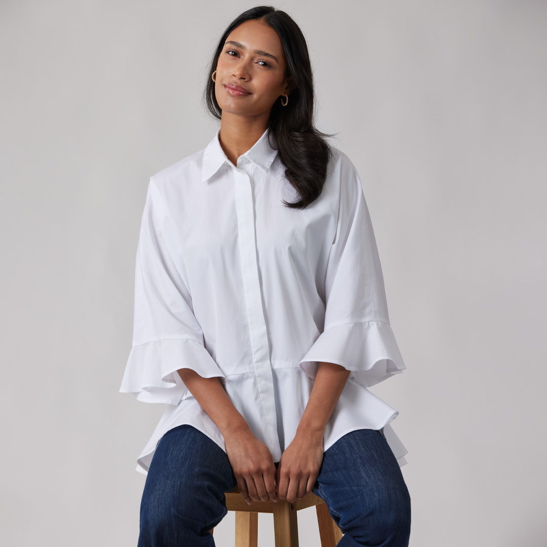 Woman sitting on a stool, wearing a white shirt and jeans.