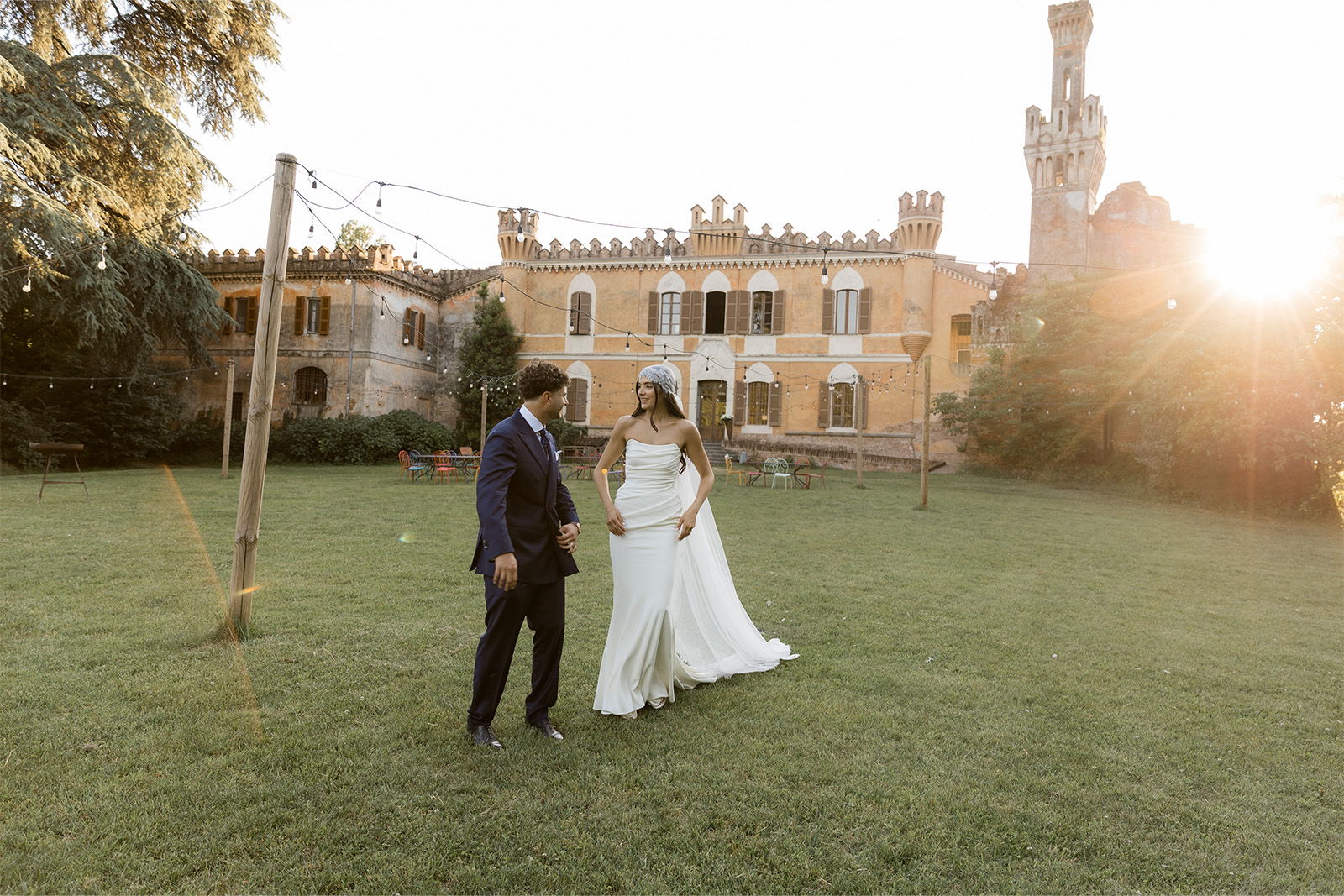 Bride and groom walking on grass in front of a castle at sunset.