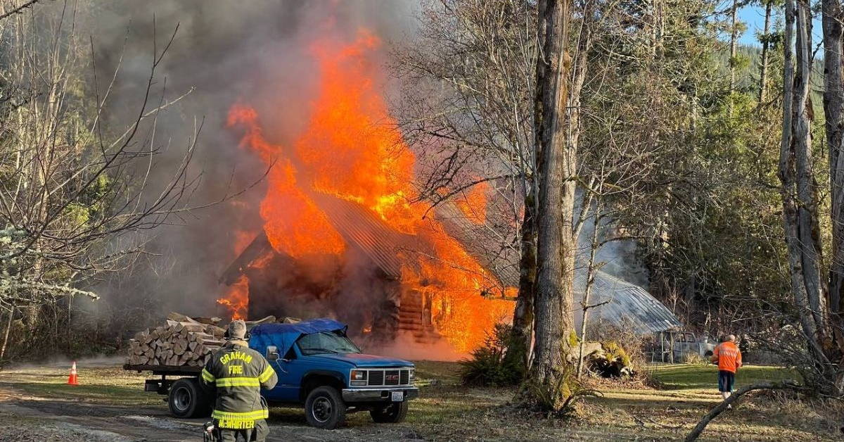 Firefighters responding to a house fire with heavy flames and smoke.