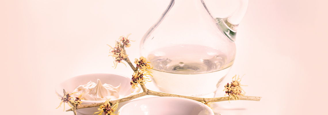 Glass decanter and bowls with flowers on a soft pink background.