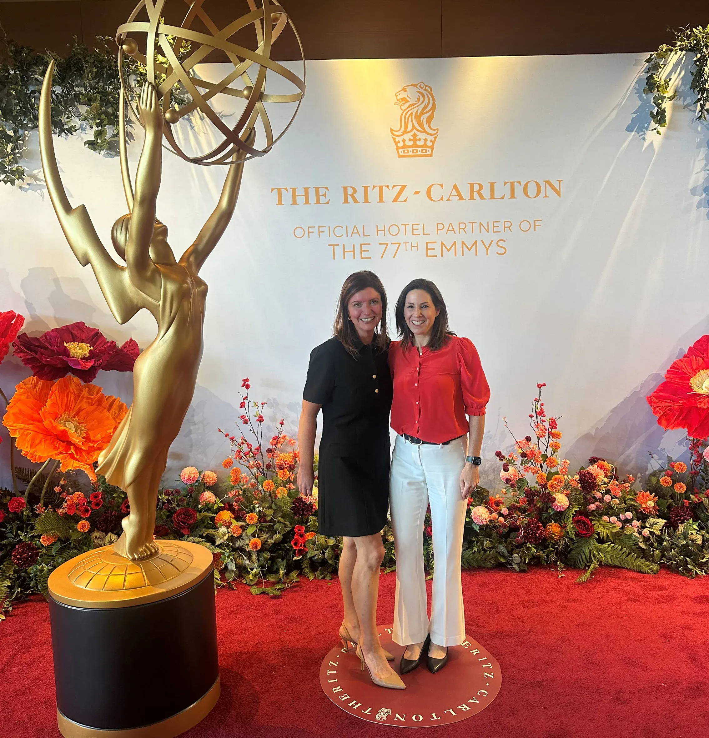 Two women posing next to an Emmy statue at a decorated event.