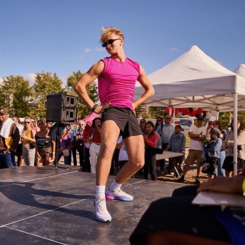 A dancer in a pink shirt performs on stage with an audience watching.