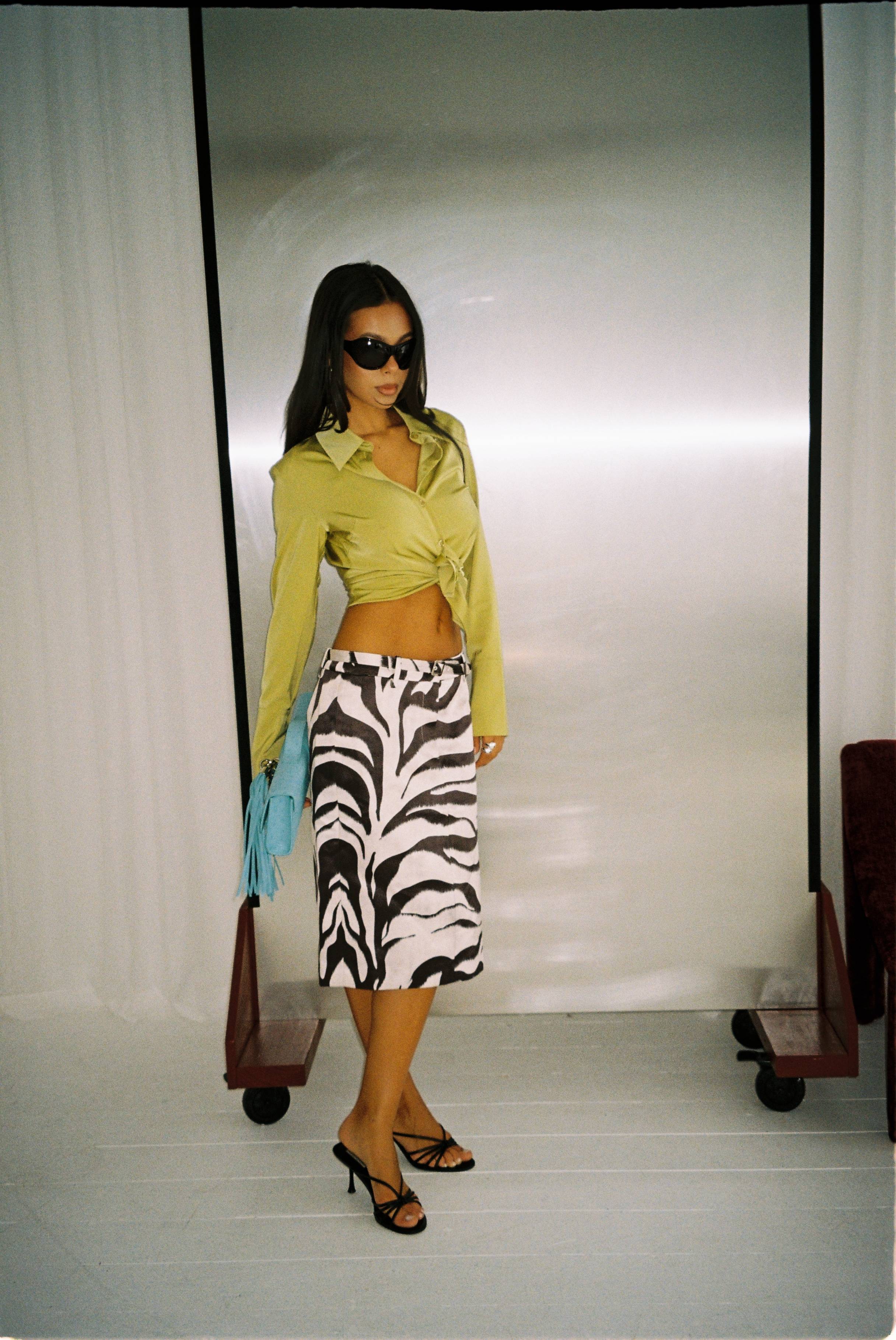 Woman in stylish outfit with zebra-print skirt and sunglasses posing indoors.