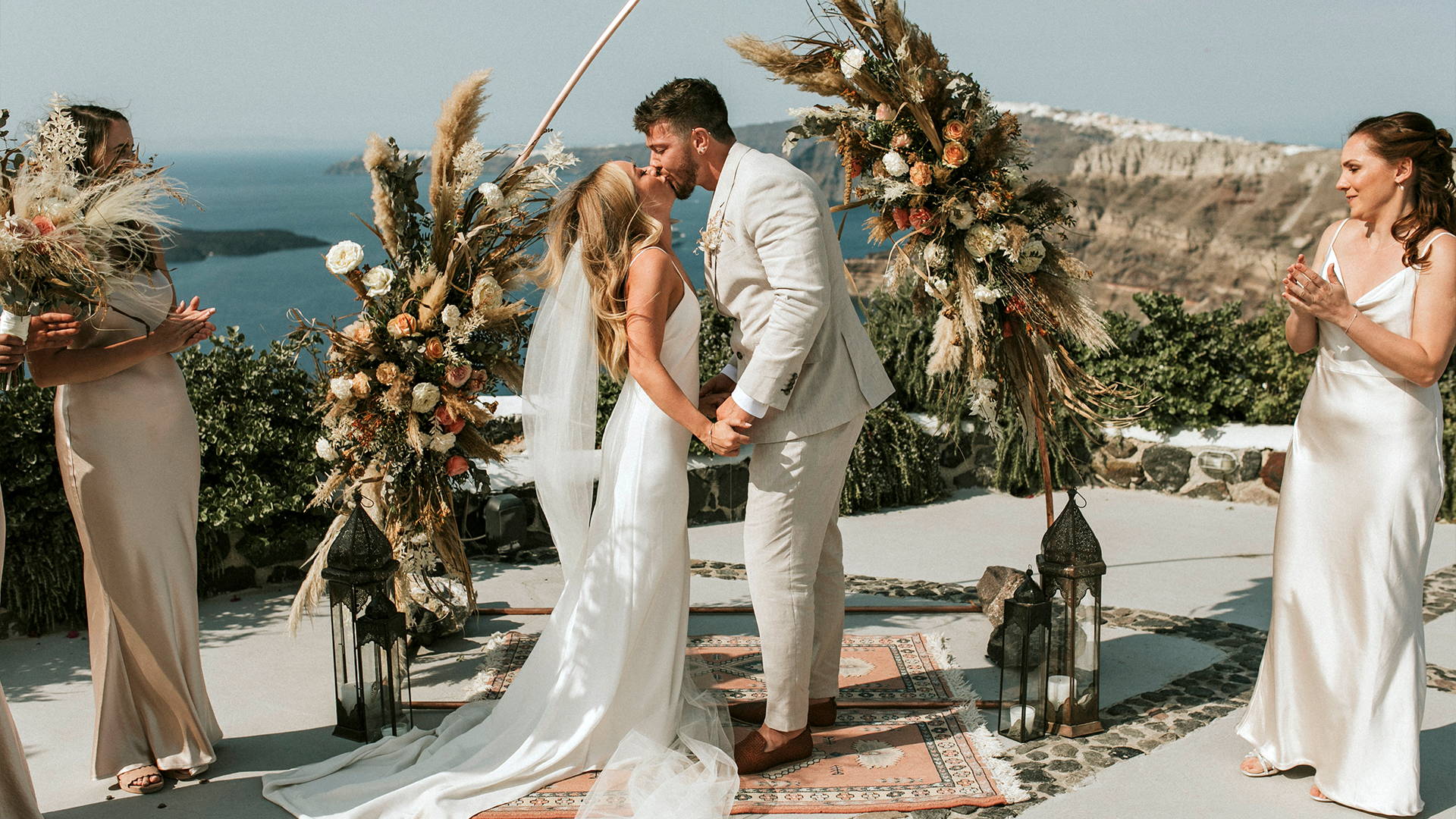 Bride and groom kissing underneath a flower arbour at the clifftop at Venetsanos Winery